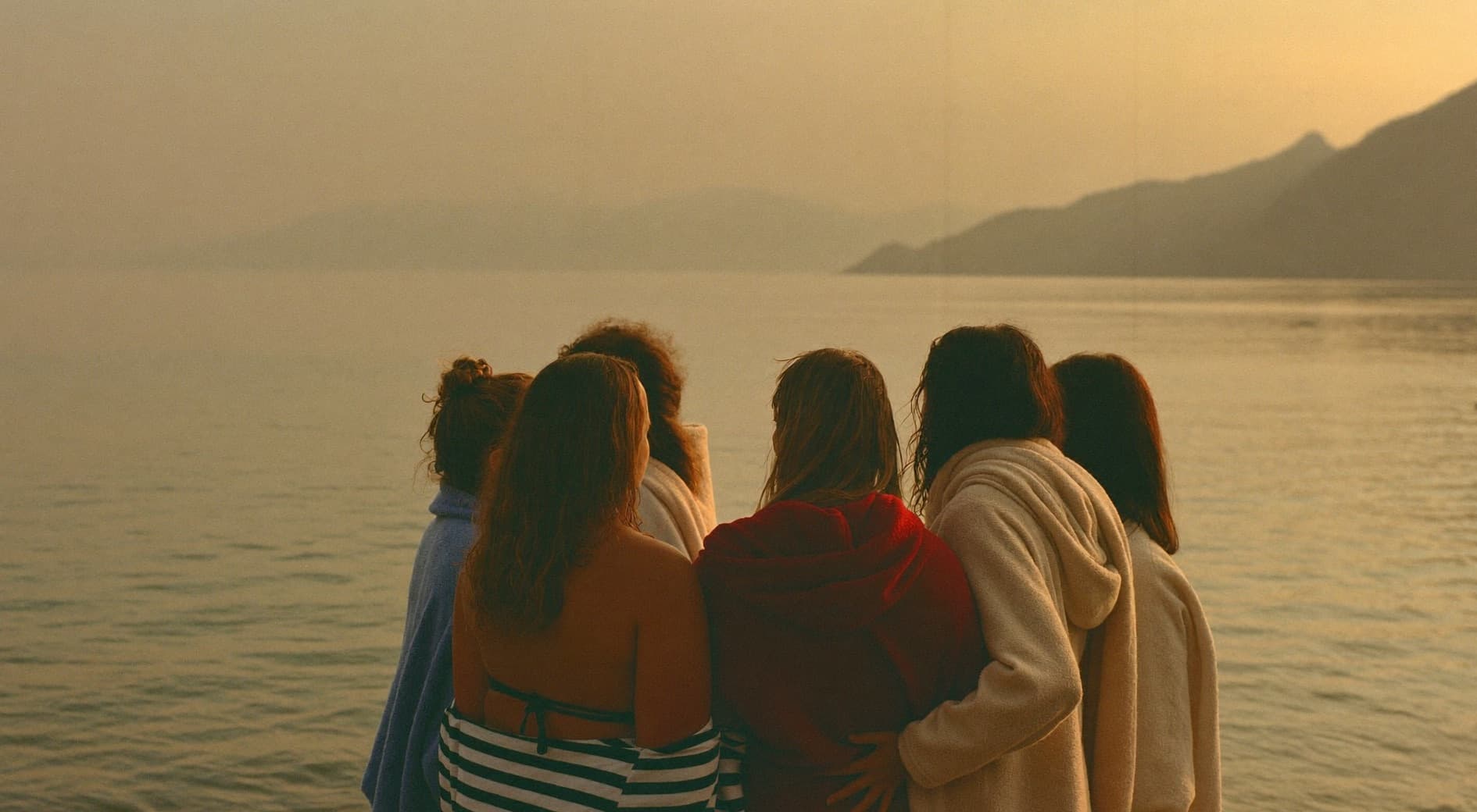 Frauen sitzen im warmen Abendlicht am Seeufer beisammen und blicken aufs Wasser